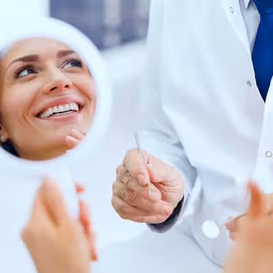 Dentist holding a dental tool while a patient smiles into a hand mirror